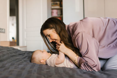 Loving mother looks at her baby lying on the bed