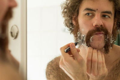 Man shaving beard while looking in mirror at home