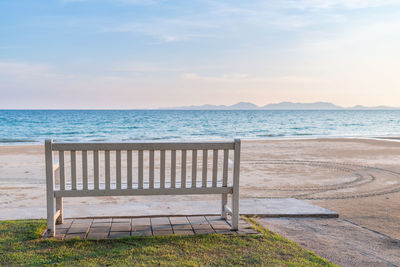 Empty bench at beach against sky during sunset