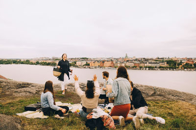 Friends greeting woman walking on field by lake against sky