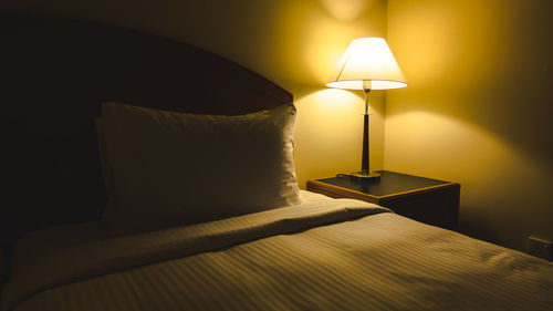 Illuminated lamp on bed against wall at home