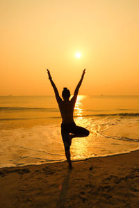 Silhouette woman exercising at beach against orange sky during sunset