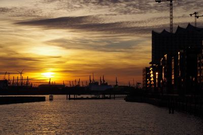 Silhouette of port and buildings against sky during sunset