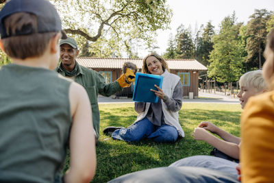 Camp counselors playing with kids while sitting on grass at summer camp