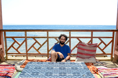 Portrait of man sitting in gazebo against sea