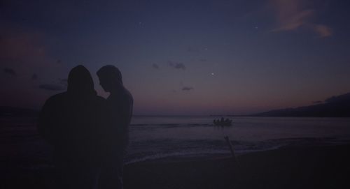 Silhouette people at beach against sky at night