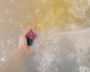Cropped hand of woman holding bath salt in bathtub