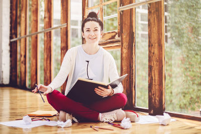 Portrait of smiling young woman sitting against window