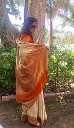 Rear view of young woman standing against tree trunk