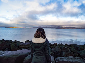 Rear view of woman standing on rock by sea against sky