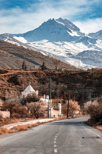 Road leading towards snowcapped mountains against sky