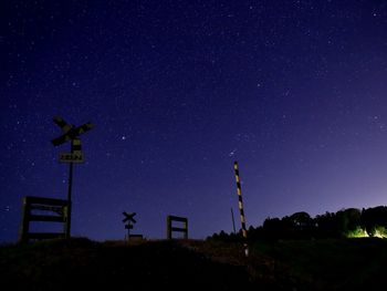 Low angle view of railroad crossing sign against star field at night