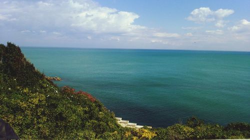 Scenic view of sea by hill against cloudy sky