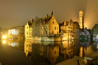 Illuminated buildings by river against sky in city at night