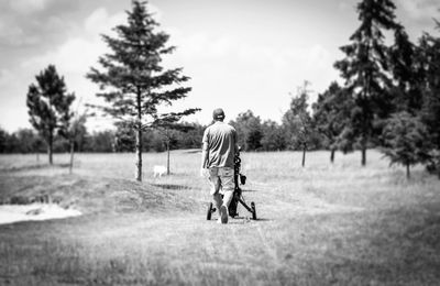 Rear view of man walking on field against sky