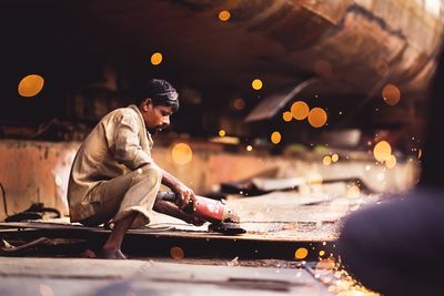 Side view of man sitting on illuminated car at night