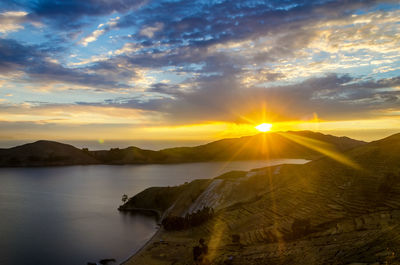 Sunbeam falling on lake and mountains against cloudy sky at sunset