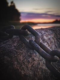 Close-up of rusty chain against sea during sunset