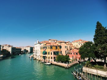 Canal amidst buildings in city against clear blue sky