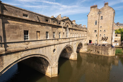 Arch bridge over river by buildings against sky