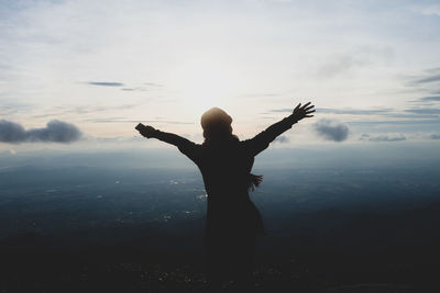 Rear view of silhouette woman with arms outstretched standing against sky