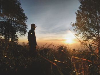 Silhouette man standing on field against sky during sunset