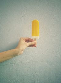 Cropped hand holding popsicle against wall