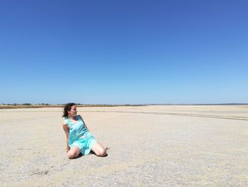 Woman sitting on sand dune against clear sky