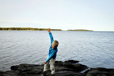 Boy standing on rock by sea against sky