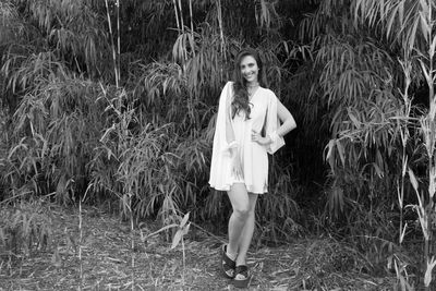 Full length portrait of smiling young woman standing against trees on land