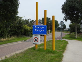 Road sign by trees against sky