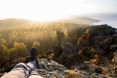 Low section of man on rock against sky during sunset