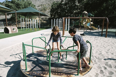 Siblings playing on carousel in playground