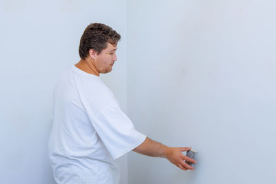 Side view of man looking away while standing against white wall