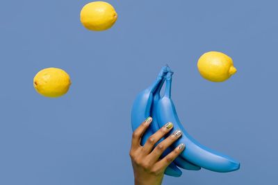 Low angle view of hand holding lemon against blue background