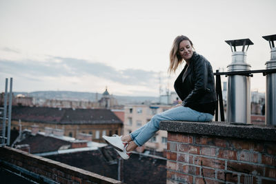 Portrait of young woman looking at cityscape against sky