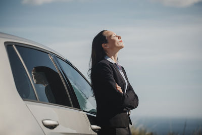 Contemplating businesswoman standing with eyes closed and arms crossed by car