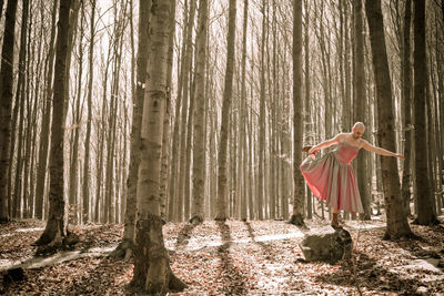 Woman standing by tree trunk in forest