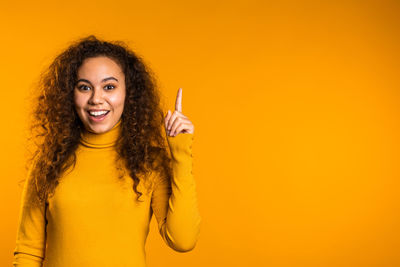 Portrait of smiling young woman against yellow background