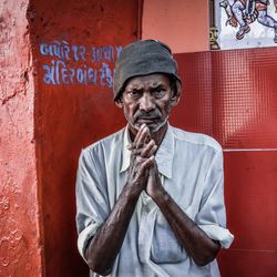 Portrait of serious senior man with hands clasped standing against red wall