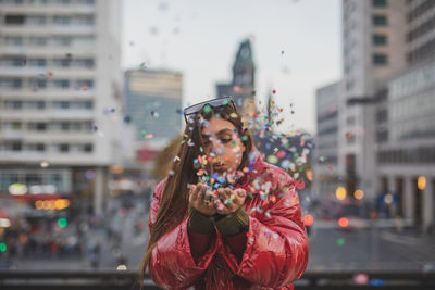 Young woman blowing colorful confetti in city during sunset