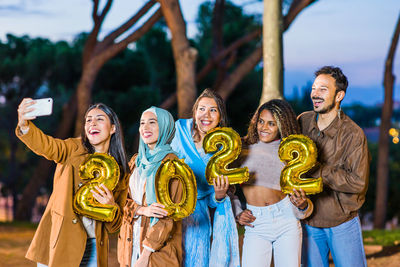 Cheerful friends holding balloon while taking selfie