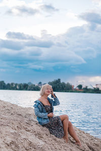 Rear view of woman sitting on beach against sky