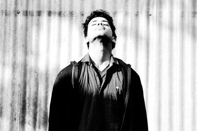 Young man with eyes closed standing against corrugated wall