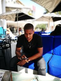 Young man using mobile phone while sitting on sofa at sidewalk cafe