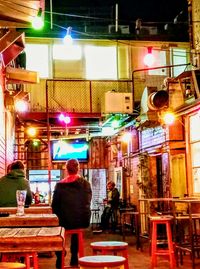 Rear view of people sitting on illuminated street at night