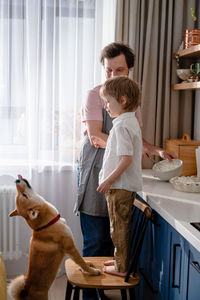 Family fun in the kitchen. cute little boy making whipped cream with his dad and furry friend