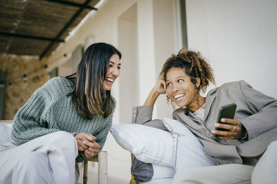 Cheerful woman sharing smart phone with friend at backyard