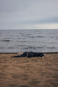 Young woman relaxing on sand at beach against sky