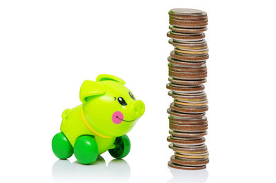 Close-up of green toy by stacked coins against white background